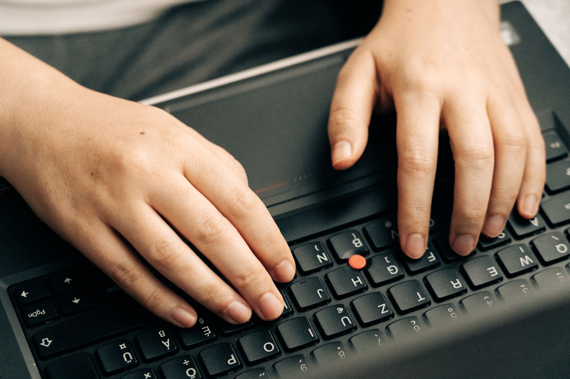 Close-up van handen die typen op het toetsenbord van een zwarte laptop.